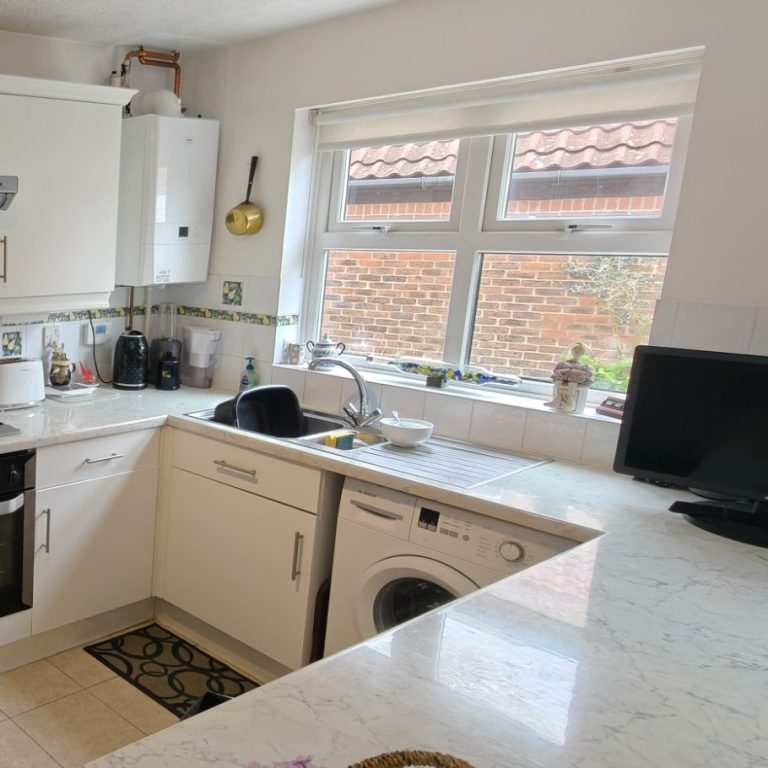Jamie's kitchen Modern kitchen with white cabinets, a sink, washing machine, and a window overlooking a garden.