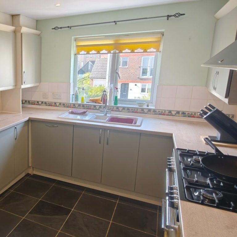 Emma's review Bright kitchen with grey cabinets, sink, and gas stove, featuring a window with yellow blinds.