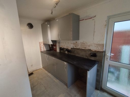 A minimalist kitchen with grey cabinets and a black countertop, partially renovated.