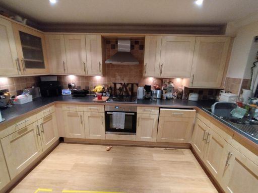 Modern kitchen with wooden cabinets, grey countertops, appliances, and various utensils.