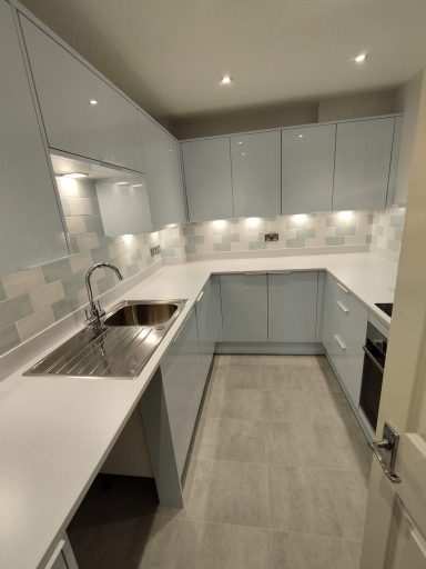 Modern kitchen with light blue cabinets, stainless steel sink, and grey flooring.