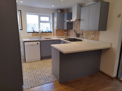 Modern kitchen with grey cabinets, white countertops, and a tiled floor.