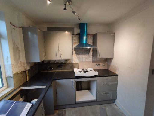 Modern kitchen with grey cabinets, black countertop, and stainless steel appliances.