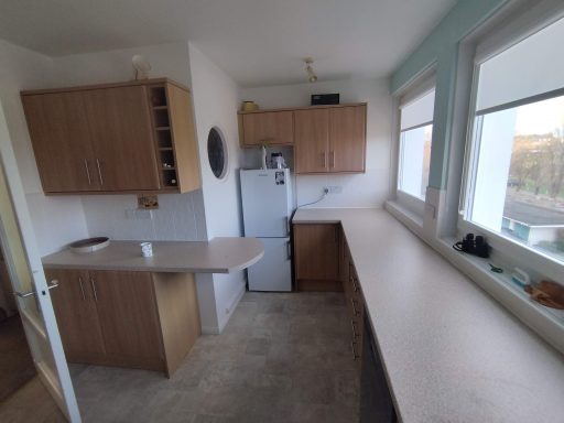 A modern kitchen with wood cabinets, a fridge, and a spacious countertop.