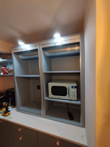 Microwave inside an open shelf unit with two shelves and under-cabinet lighting.
