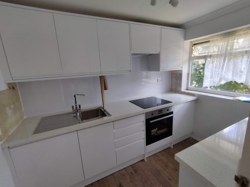 Modern white kitchen with a sink, stove, and large window letting in natural light.