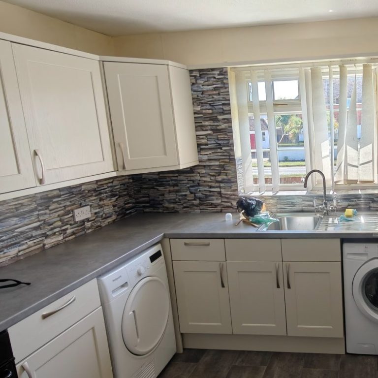 replacement doors Modern kitchen with white cabinets, grey countertop, and a washing machine. Natural light through the window.