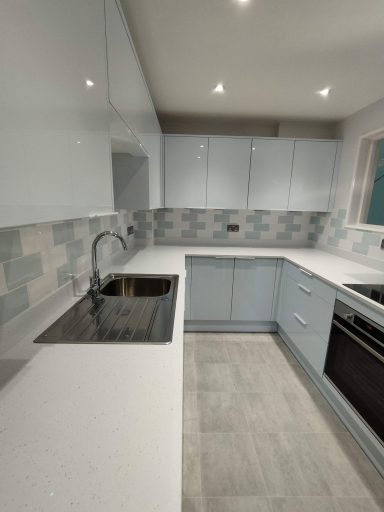 Modern kitchen with light blue cabinets, a stainless steel sink, and grey tile backsplash.