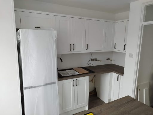 Modern kitchen with white cabinets, a refrigerator, and wooden countertops.