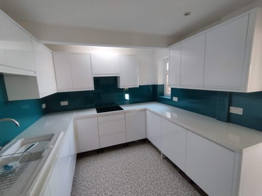 Modern kitchen with white cabinetry and teal tiled backsplash. Bright and spacious layout.