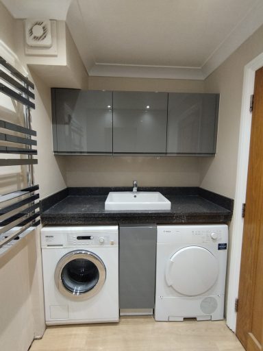 Laundry area featuring a washing machine, dryer, sink, and grey cabinets.