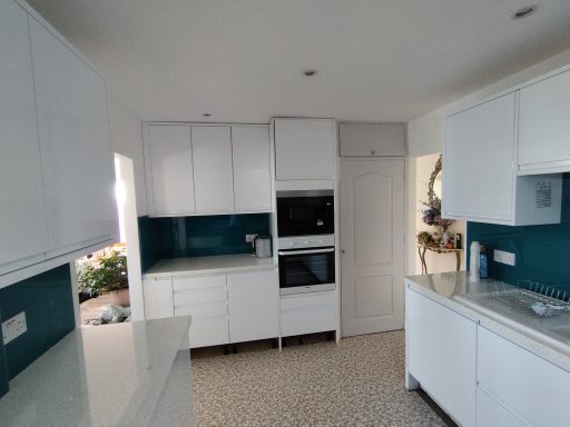 Modern kitchen with white cabinets, blue backsplash and integrated appliances.