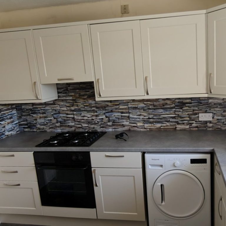Replacement fronts and tops Modern kitchen with cream cabinets, stone backsplash, gas hob, and a washing machine.