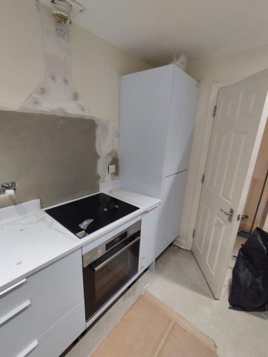 A kitchen showing a white fridge, oven, sink, and unfinished wall beside a closed door.