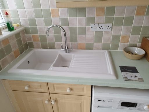 A clean kitchen sink with a mixer tap and a tiled backsplash.