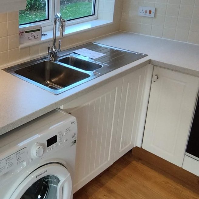 Worktop replacement A modern kitchen with a double sink, washing machine, and white cabinetry.