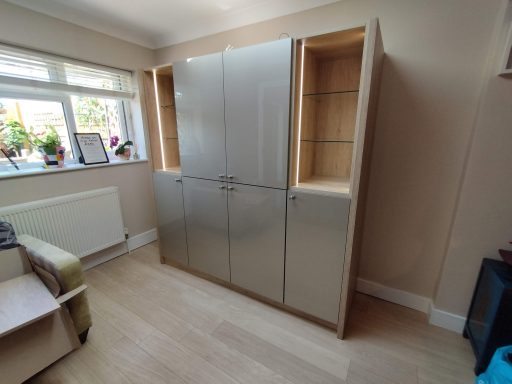 Modern wooden storage cabinet with glass doors, situated in a bright, tidy room.