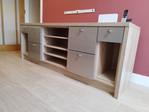 Modern wooden sideboard with grey drawers and open shelving against a red wall.