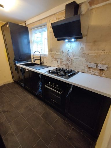 Modern kitchen with black cabinetry, gas stove, and stainless steel extractor hood against a textured wall.