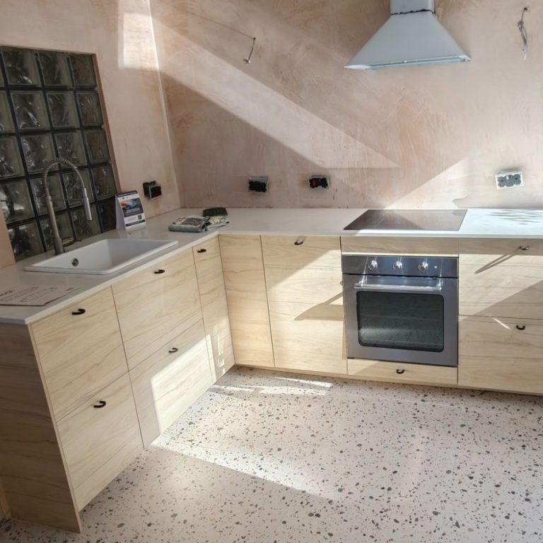 kitchen ready for tiles Modern kitchen with wooden cabinets, oven, and sunlight streaming through a window.