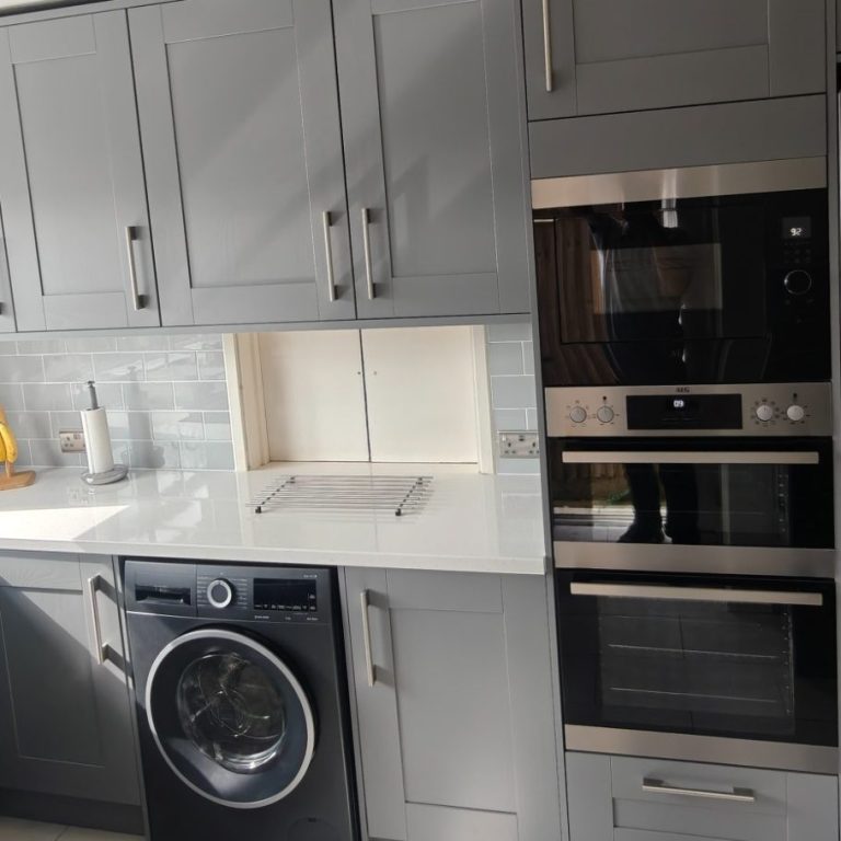 grey kitchen Modern kitchen featuring grey cabinets, a washing machine, and built-in ovens.