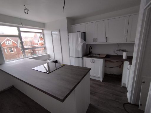 Modern kitchen with white cabinets, grey countertops, and large windows overlooking houses.