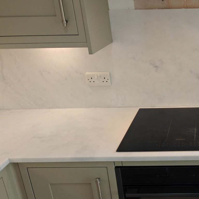 Acrylic worktop and splashback A modern kitchen countertop with a hob, cabinets, and white marble backsplash.