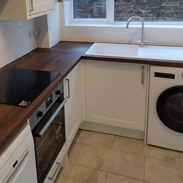Laminate worktop Modern kitchen corner featuring a black hob, oven, sink, and washing machine.