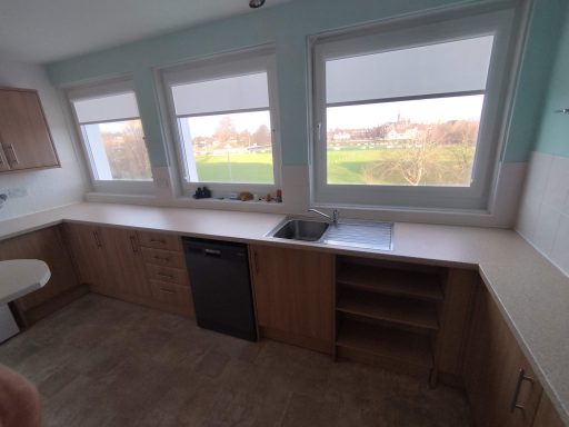 Modern kitchen with wooden cabinetry, a sink, and windows overlooking greenery.