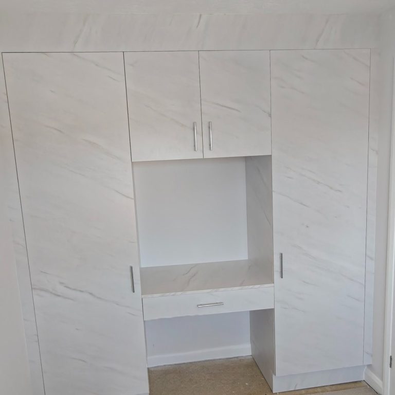 Wardrobes and dressing table White cabinetry with a central desk and storage, placed against a bright wall.