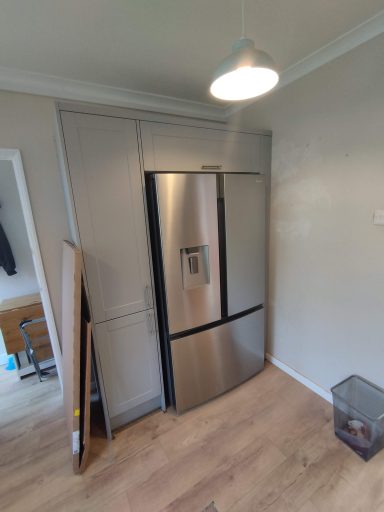 Modern stainless steel fridge installed in a fitted kitchen with wooden flooring.